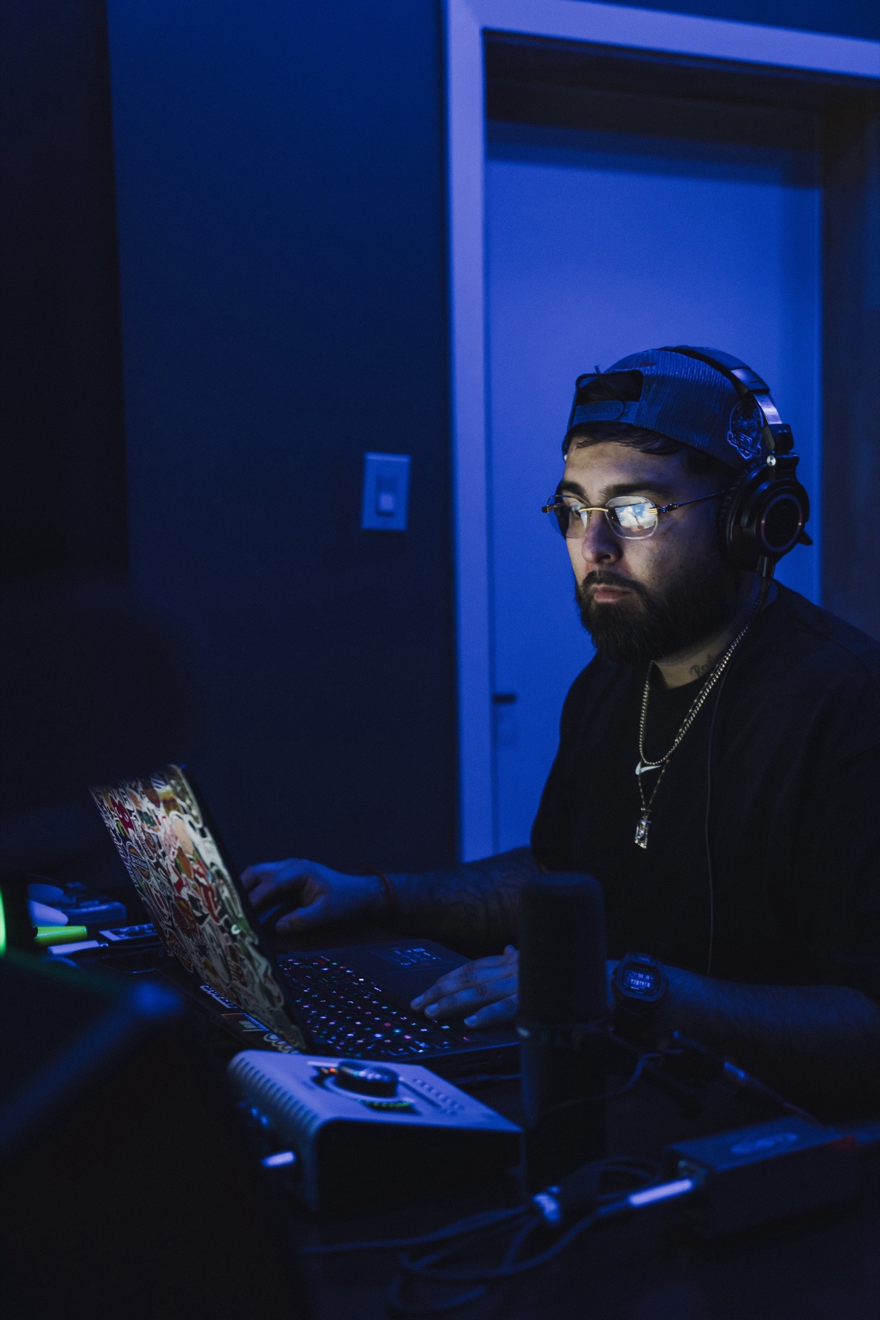 The beatmaker at the laptop, headphones on — blue ambient light