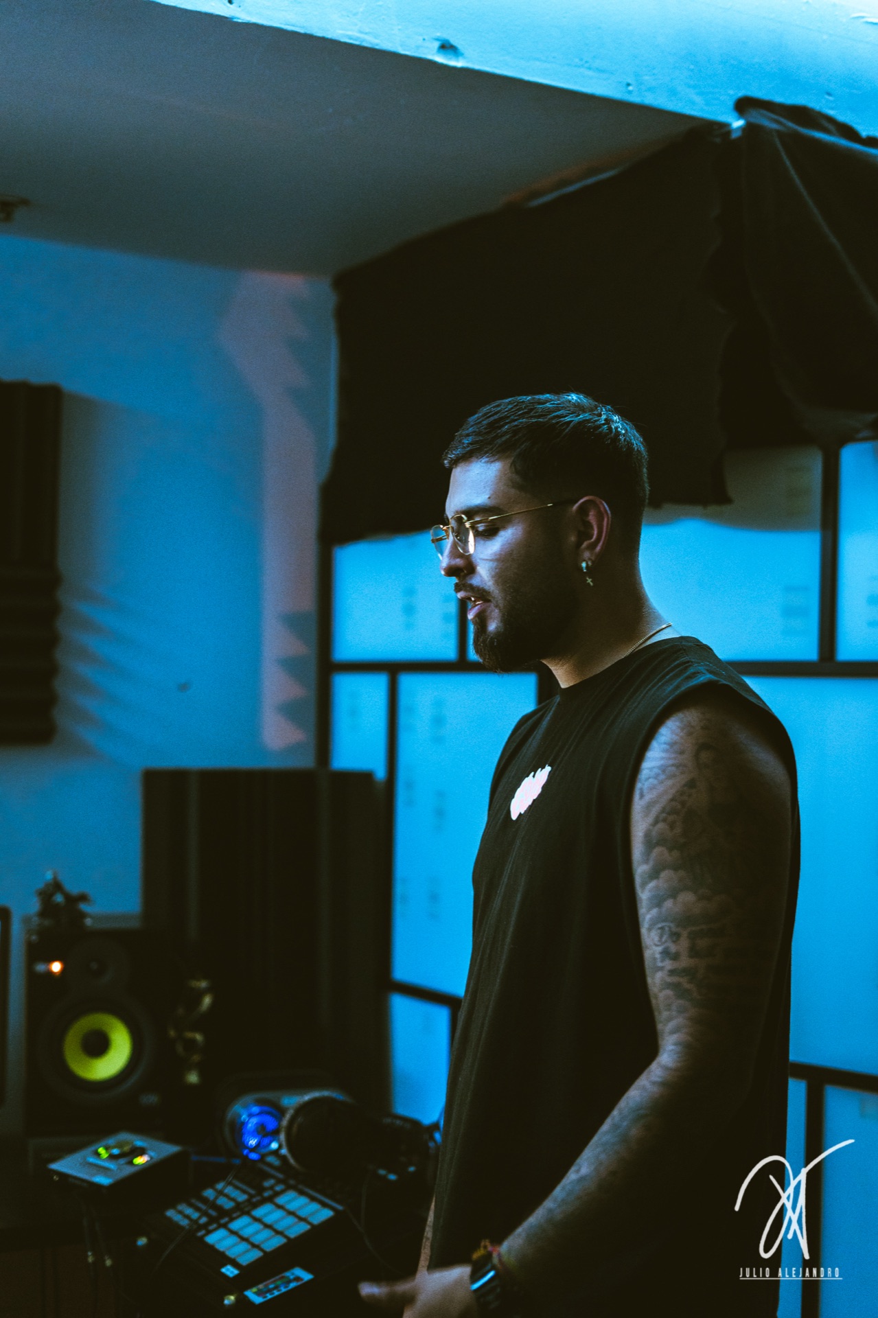 The beatmaker at the MPC — blue light, tattooed arm, gear in focus